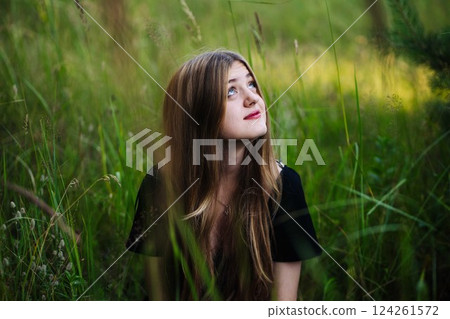 Woman contemplating, standing in tall green grass, wearing black dress, embracing serene natural landscape 124261572