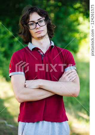 Confident young man standing outdoors, crossing arms with relaxed posture, embodying casual style and self assurance 124261575