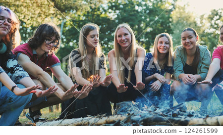 Group of young students enjoying a summer camp, warming their hands by the campfire in a forest Group of young students enjoying a summer camp, warming their hands by the campfire in a forest 124261599