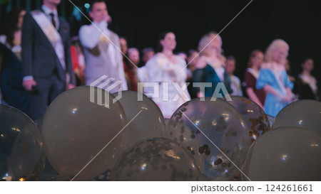 Graduation celebration featuring white balloons, floating confetti, blurred graduates standing on stage commemorating academic success 124261661