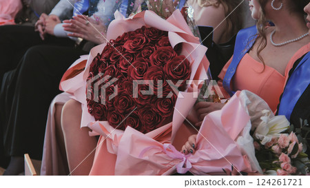 Graduate student holding large red rose bouquet, commemorating academic success during graduation celebration, expressing personal triumph 124261721