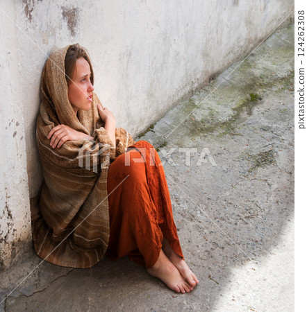 A girl in poor clothes sits on the ground A girl in poor clothes sits on the ground 124262308