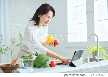 A middle-aged woman cooking while looking at a recipe on a tablet A middle-aged woman cooking while looking at a recipe on a tablet 124262363