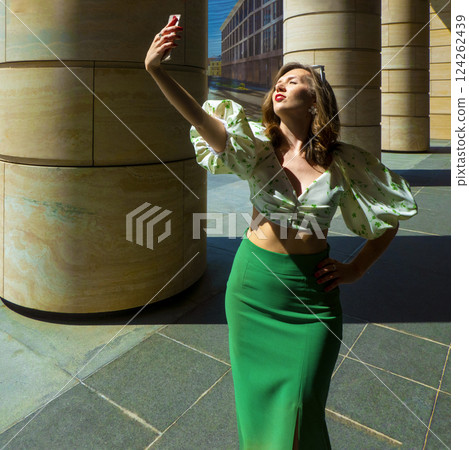 Joyful young caucasian woman winks, bites her tongue, takes selfie on phone. Blonde model wears hat in sunny weather. Positive emotions concept 124262439