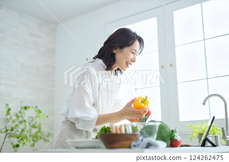 A middle-aged woman cooking while looking at a recipe on a tablet A middle-aged woman cooking while looking at a recipe on a tablet 124262475