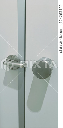 A stainless steel door handle is mounted on a fresh white door, showcasing a clean and modern design. The sleek finish creates a sophisticated look suitable for contemporary interiors. 124263133