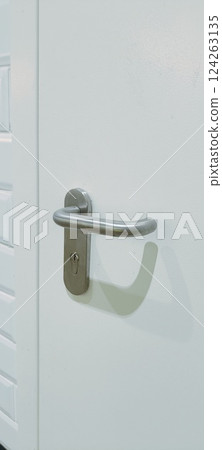 A white door stands against a backdrop of glossy white tiles and black lower wall tiles. The door features a contemporary handle, enhancing the minimalistic decor of the area 124263135