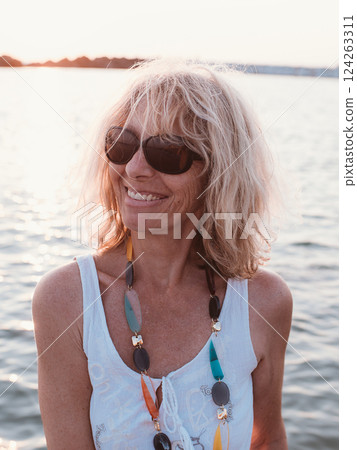 Woman Smiling Wearing Sunglasses by the Water at Sunset Woman Smiling Wearing Sunglasses by the Water at Sunset 124263311