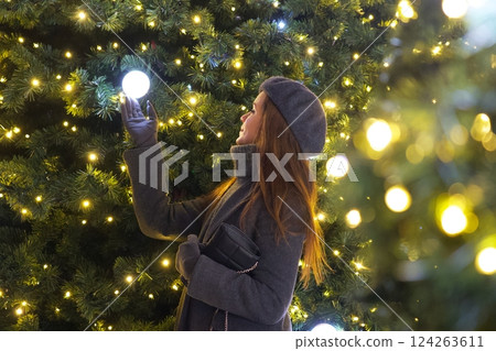 Elegant Parisian girl near Christmas tree gazing at festive decorations  124263611