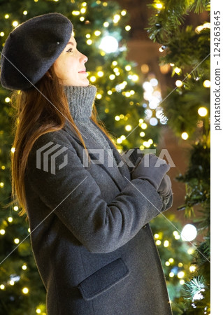 Parisian girl in grey coat admires New Year decorations by Christmas tree Parisian girl in grey coat admires New Year decorations by Christmas tree 124263645