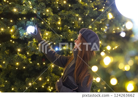 Elegant Parisian girl near Christmas tree gazing at festive decorations Elegant Parisian girl near Christmas tree gazing at festive decorations 124263662