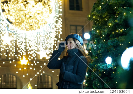 Happy Parisian girl near Christmas tree admires festive New Year ornaments Happy Parisian girl near Christmas tree admires festive New Year ornaments 124263664