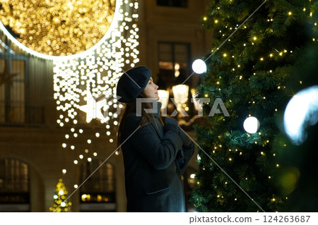 Festive Parisian girl in beret and coat admiring Christmas tree decorations Festive Parisian girl in beret and coat admiring Christmas tree decorations 124263687