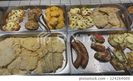 Cooked fish, breaded cutlets and chicken breasts resting in metal trays, ready to be served 124264009