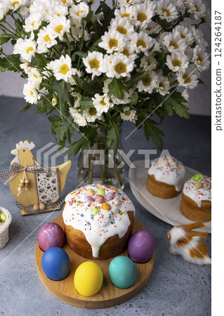 Easter kulich with candied fruits in white glaze with colorful sprinkles and painted eggs. Traditional Easter pastry. Easter holiday. Close-up, selective focus. 124264187