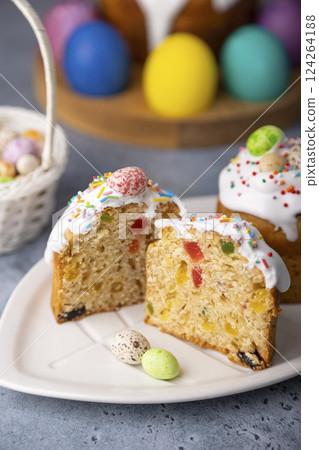 Two small Easter kulichs with candied fruits in white glaze with colorful sprinkles in the cut. Painted chicken and quail eggs. Traditional Easter baking. Easter holiday. Close-up, selective focus. 124264188
