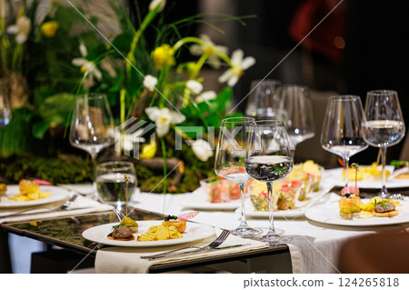 Luxurious dining table setup featuring gourmet appetizers, elegant glassware, floral centerpiece Luxurious dining table setup featuring gourmet appetizers, elegant glassware, floral centerpiece 124265818