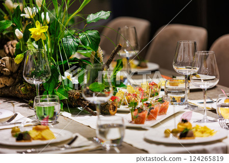 Luxurious dining table setup featuring gourmet appetizers, elegant glassware, floral centerpiece Luxurious dining table setup featuring gourmet appetizers, elegant glassware, floral centerpiece 124265819