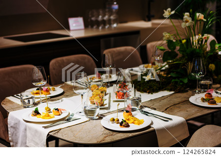 Luxurious dining table setup featuring gourmet appetizers, elegant glassware, floral centerpiece 124265824