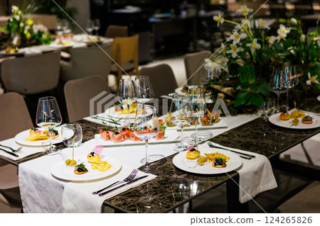 Luxurious dining table setup featuring gourmet appetizers, elegant glassware, floral centerpiece 124265826