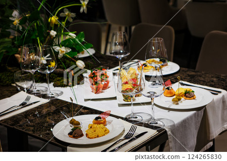 Luxurious dining table setup featuring gourmet appetizers, elegant glassware, floral centerpiece 124265830