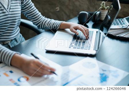 A person working on a laptop while reviewing financial documents, showcasing a professional office environment. 124266046