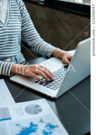 A business professional working on a laptop in a modern office setting, with data charts visible on the desk. A business professional working on a laptop in a modern office setting, with data charts visible on the desk. 124266047