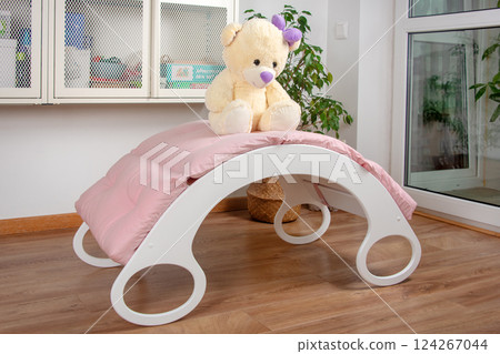 White wooden rocking bed adorned with pink cushions in a cozy indoor setting. Kids rocking bed placed in a warmly lit corner of a room with natural flooring and indoor decor White wooden rocking bed adorned with pink cushions in a cozy indoor setting. Kids rocking bed placed in a warmly lit corner of a room with natural flooring and indoor decor 124267044