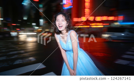 A flash-lit shot of a young woman wearing an elegant dress, in the middle of a busy city at night. Youth and happiness concept 124267141