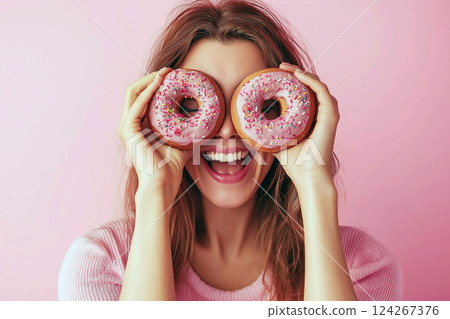 Happy woman holding colorful donuts playfully against her face, like a glasses. Donut binoculars. Diet, sweets, sugar free dessert concept, dieting, junk food, slimming, weight loss 124267376