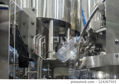 The  empty drinking water bottles  hanging on the conveyor belt for filling process. 124267503