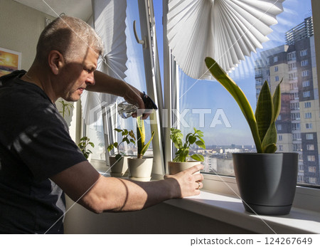 Man spraying indoor plants on the windowsill Man spraying indoor plants on the windowsill 124267649