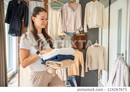 A young woman holds a stack of clothing in her hands, sorting items for resale, donation, or recycling. Sustainable fashion and second-hand use help reduce waste and promote conscious consumption 124267673