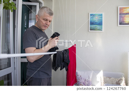 Man hangs the clothes on the roller dryer on the balcony Man hangs the clothes on the roller dryer on the balcony 124267760