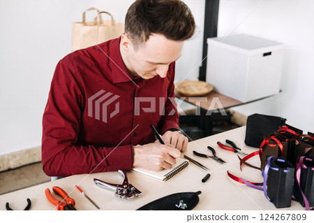 Male solo entrepreneur journaling in a creative studio surrounded by handmade packaging and tools. Work-Life Balance for Creative Professionals, mindful work, personal fulfillment. Male solo entrepreneur journaling in a creative studio surrounded by handmade packaging and tools. Work-Life Balance for Creative Professionals, mindful work, personal fulfillment. 124267809