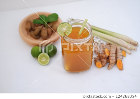 Fresh ginger and lemon juice in a glass jar with ginger roots on white background. Fresh ginger and lemon juice in a glass jar with ginger roots on white background. 124268354