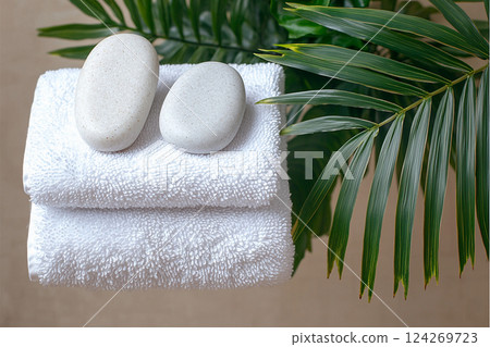 Soft white towels are neatly stacked, accompanied by smooth, pale stones, all set against vibrant green palm leaves, creating a calming atmosphere Generative AI 124269723