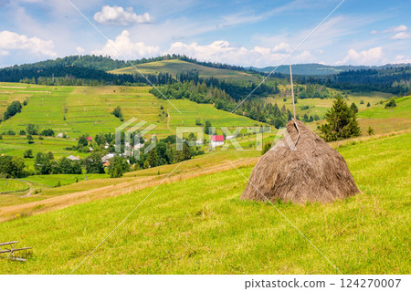 rural landscape in summer. countryside scenery with haystack on the field beneath a blue sky with clouds. carpathian village in the distance rural landscape in summer. countryside scenery with haystack on the field beneath a blue sky with clouds. carpathian village in the distance 124270007