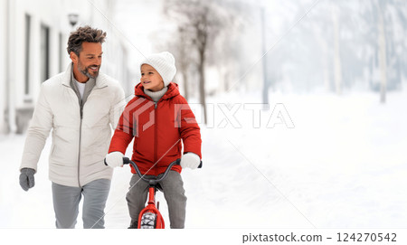 sunny winter day father teaches son to ride a bike, smiling boy riding a red bike, father helps and supports son, family happiness concept, copy space for father's day poster 124270542
