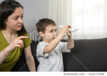 A boy studies a figurine of a passenger plane with his mother. Education and study of vehicles. Learning about aviation and vehicle mechanics. Curiosity about travel, engineering, how planes operate. 124271089