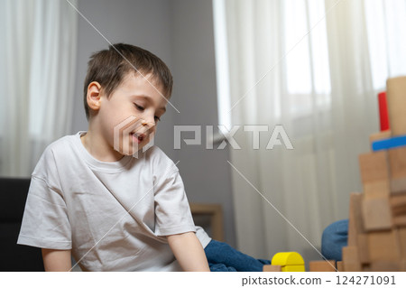Little boy playing with wooden blocks on the floor. Games at home. Encouraging hands-on learning, focus, and motor skill development through interactive play. Developing creativity 124271091