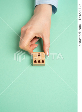 A hand holds a block with a symbol of hierarchy in a company or community. Leadership, organizational structure, and team coordination in businesses or communities. A hand holds a block with a symbol of hierarchy in a company or community. Leadership, organizational structure, and team coordination in businesses or communities. 124271126