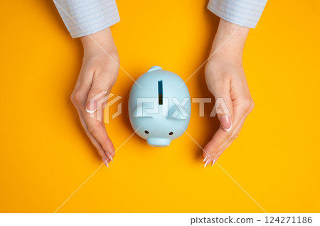 The piggy bank is protected by the hands of a woman in a protective gesture. Safeguarding personal savings, ensuring financial stability, and protecting assets. 124271186