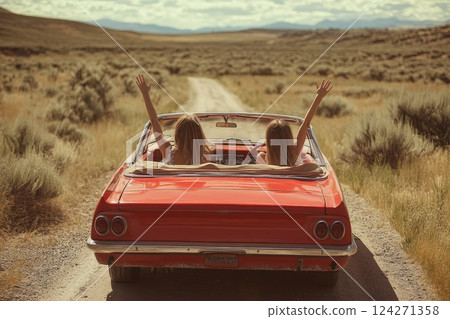 Two girls in a red car with their hands up driving through a valley in summer 124271358