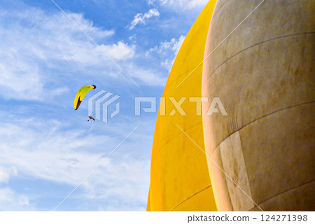 Paragliding in a blue sky with clouds and a yellow hot air balloon in the background. 124271398