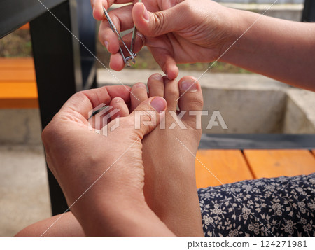 Mother carefully trimming her kid's toenails using a nail clipper, ensuring hygiene and foot health Mother carefully trimming her kid's toenails using a nail clipper, ensuring hygiene and foot health 124271981