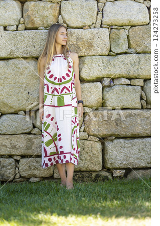 Young woman wearing summer dress leaning against stone wall Young woman wearing summer dress leaning against stone wall 124273258