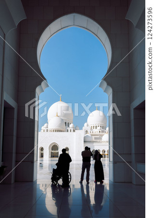 View of Sheikh Zayed Grand Mosque in Abu Dhabi made of white marble with flowers made of precious stones in design and beautiful reflections. Silhouettes of tourists admiring beauty of art. Vertical 124273596