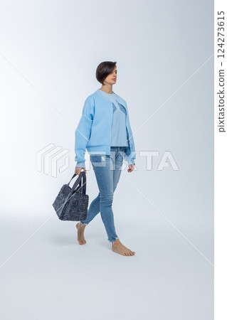 Beautiful woman of model appearance. Girl in blue clothes with black bag on grey background. Pretty female with trendy makeup posing in studio. Vertical photo. High quality photo 124273615