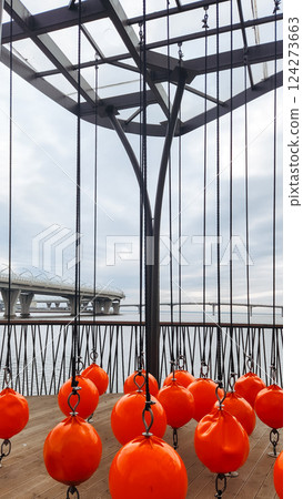 Beautifully designed recreation area on seashore. Chain swings, decorative elements in form of orange balls and wooden paths on outdoor playground. 124273663